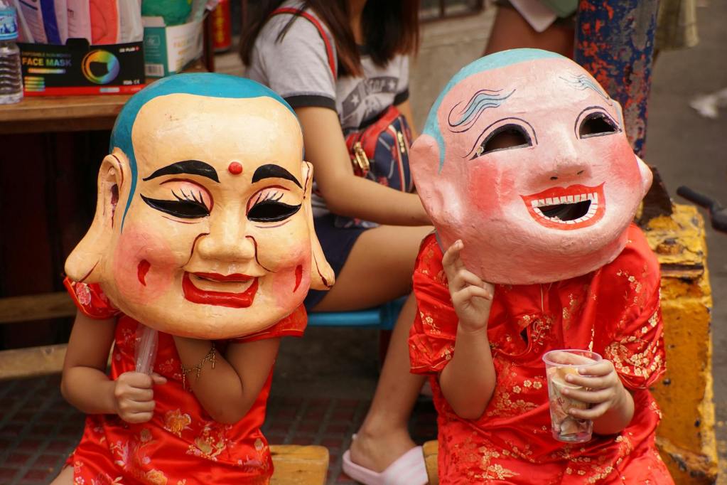 women in traditional clothing wearing buddha masks