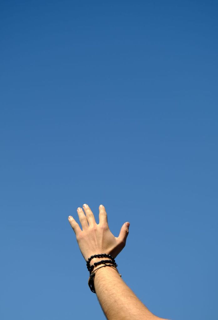 hand reaching towards a clear blue sky